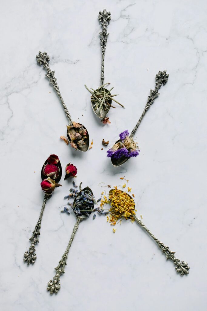 Decorative spoons with dried flowers and herbs, arranged on a light surface.