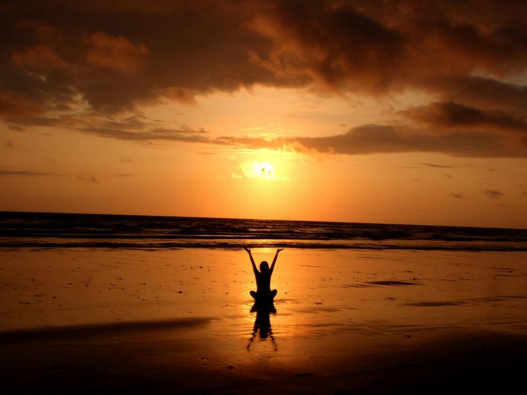 Silhouette of a person with arms raised in triumph or joy at sunset on a beach.