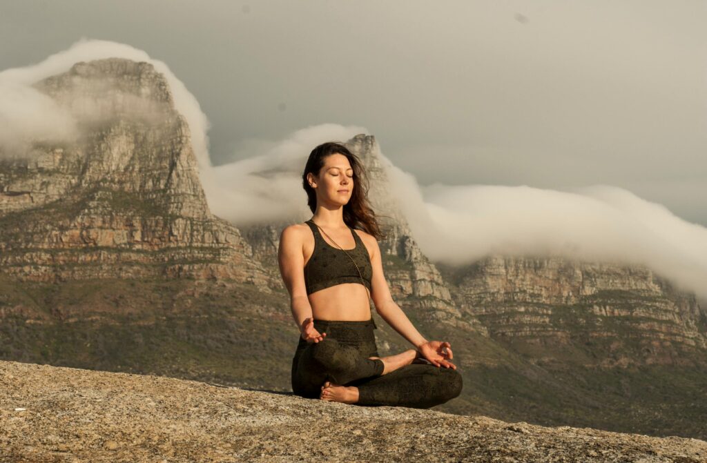 Woman meditating in lotus pose with a blurred, rugged mountain or ruin background.