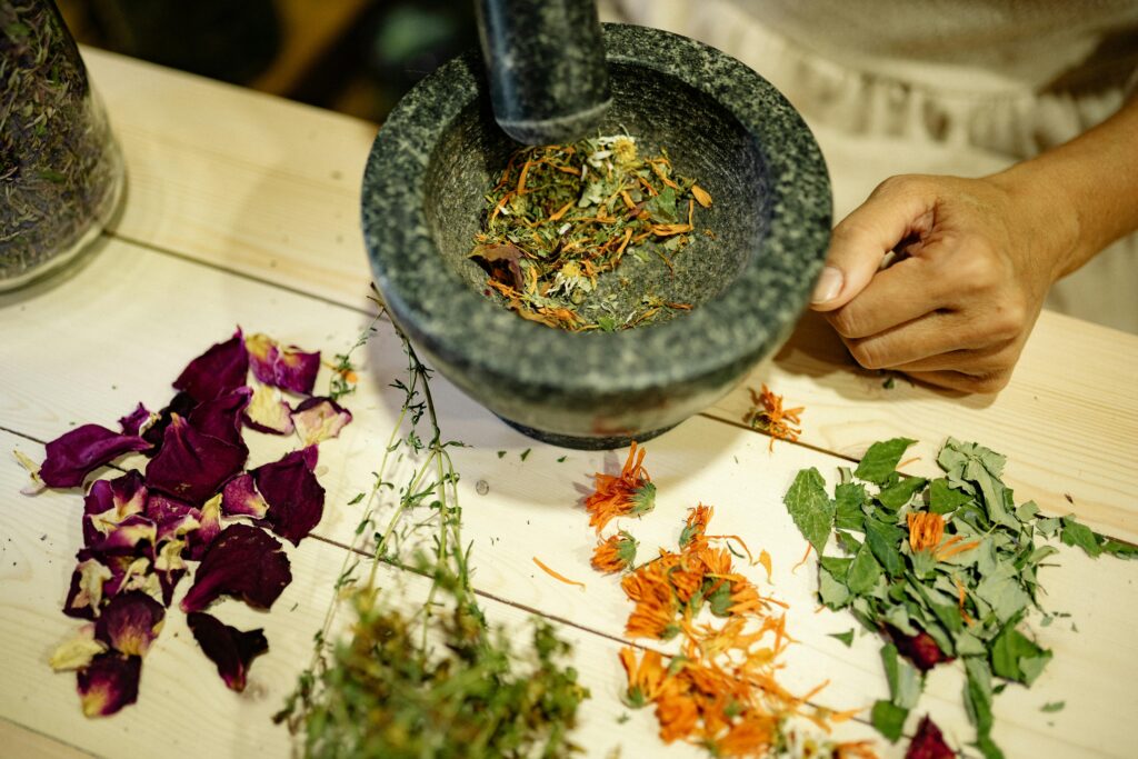 Overhead view of hands using a mortar and pestle to grind herbs, surrounded by dried flowers.