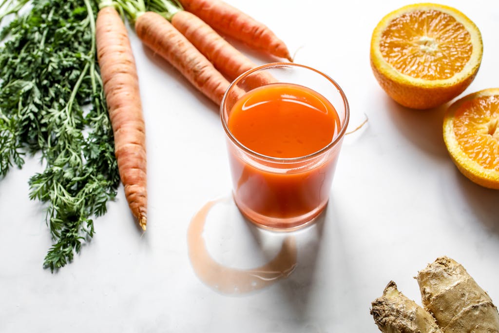 A refreshing glass of carrot, orange, and ginger juice surrounded by fresh ingredients on a white background.